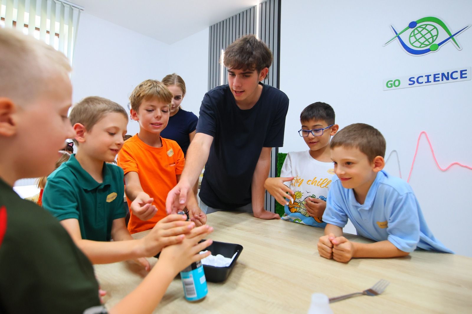 Un mentor Go Science arată un experiment unui grup de copii entuziasmați