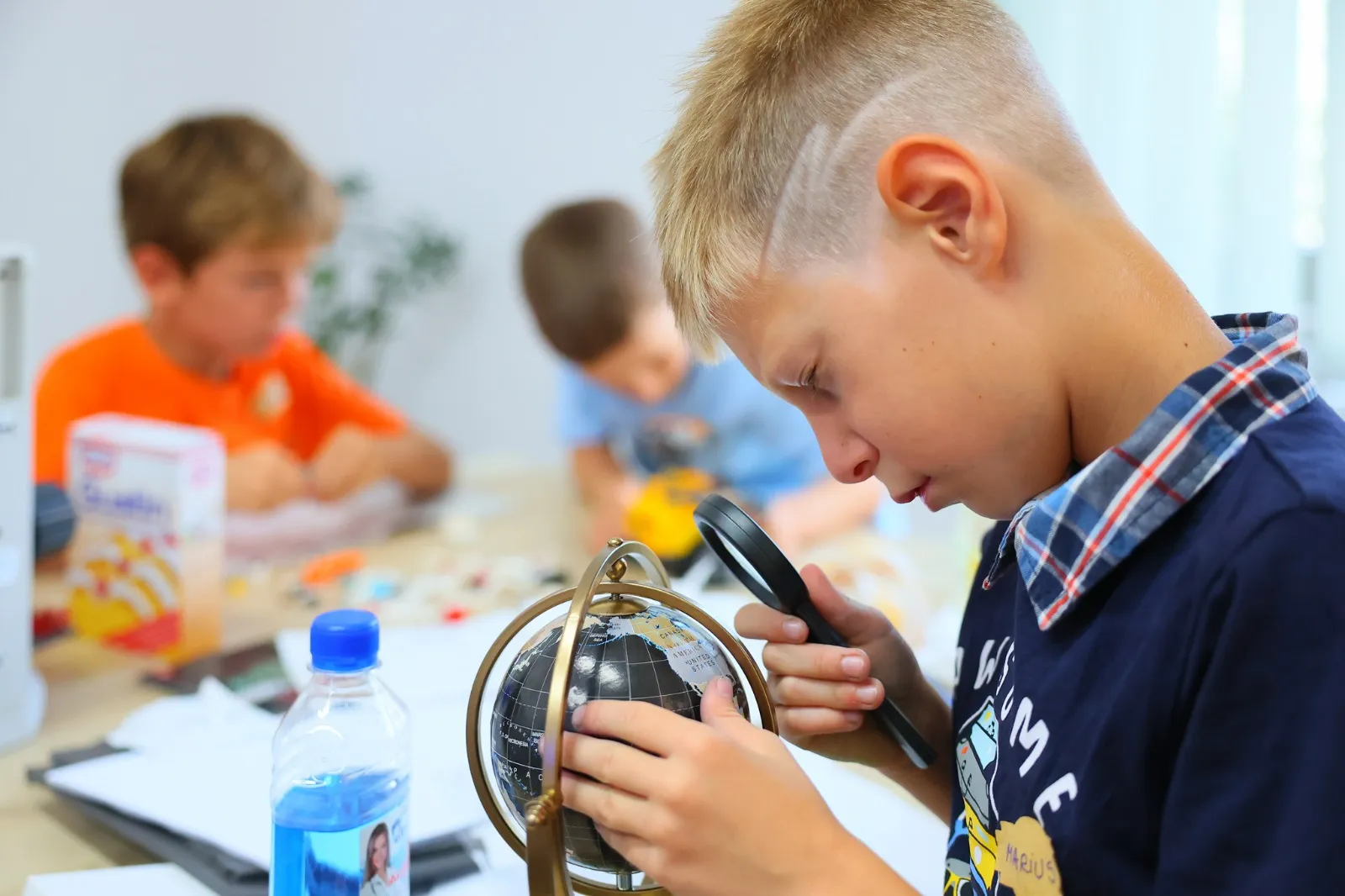 Băiat care studiază un glob cu lupa