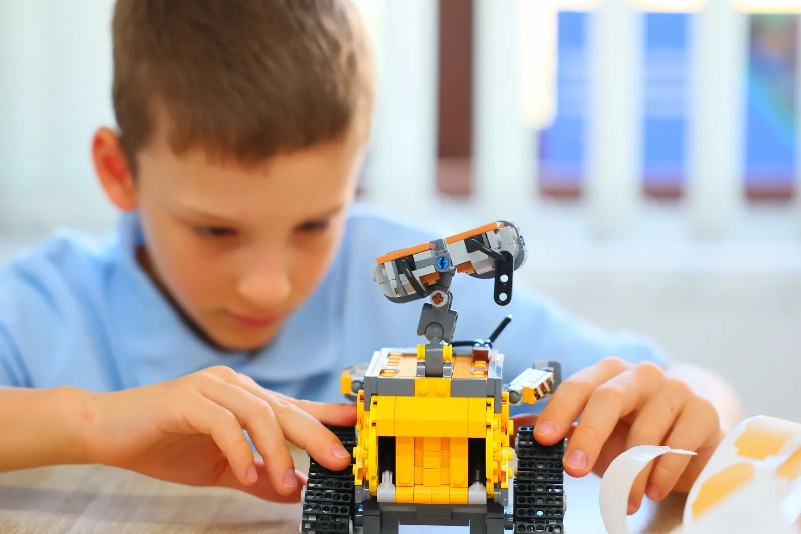 Băiat concentrat lângă robotul LEGO construit de el